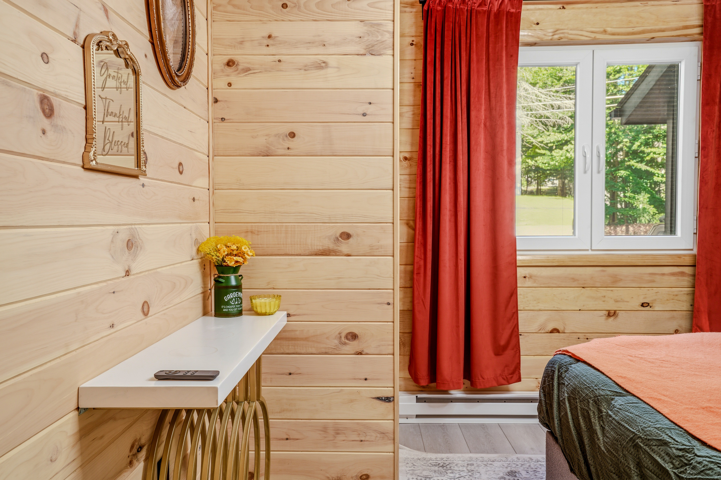 Bedroom with red curtains, natural wood walls, and a built-in shelf detail