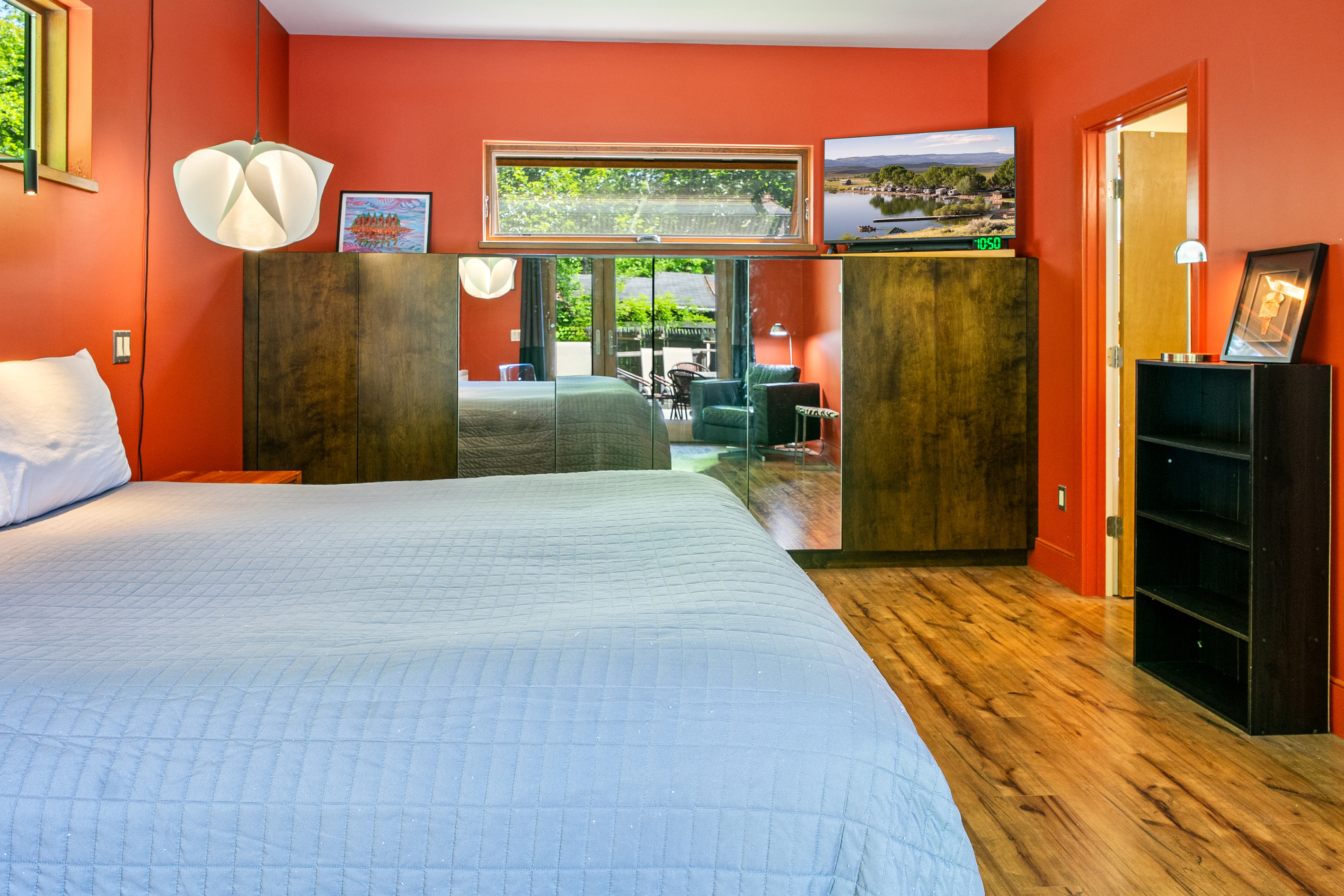 Boutique comfort in the main floor suite at "The Crag." Features bold terracotta walls, a plush bed, flat-screen TV, custom built-in armoires with full-length mirrored doors, and modern pendant lighting for a cozy night's rest.
