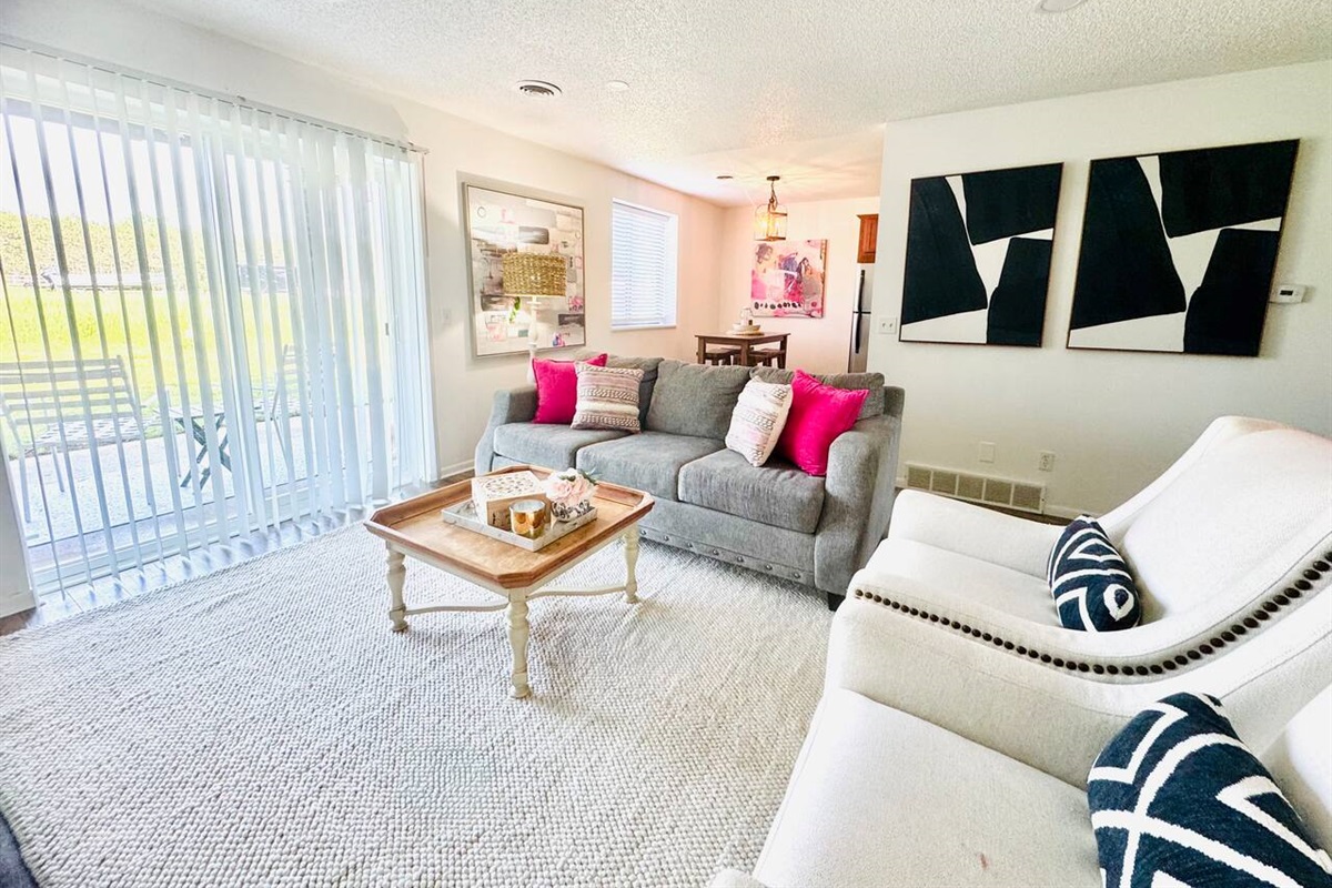 Bright and inviting living space with colorful floral decor, comfortable seating, and a playful area rug. Sliding glass doors open to scenic views, filling the room with natural light—perfect for morning coffee or evening unwinding.