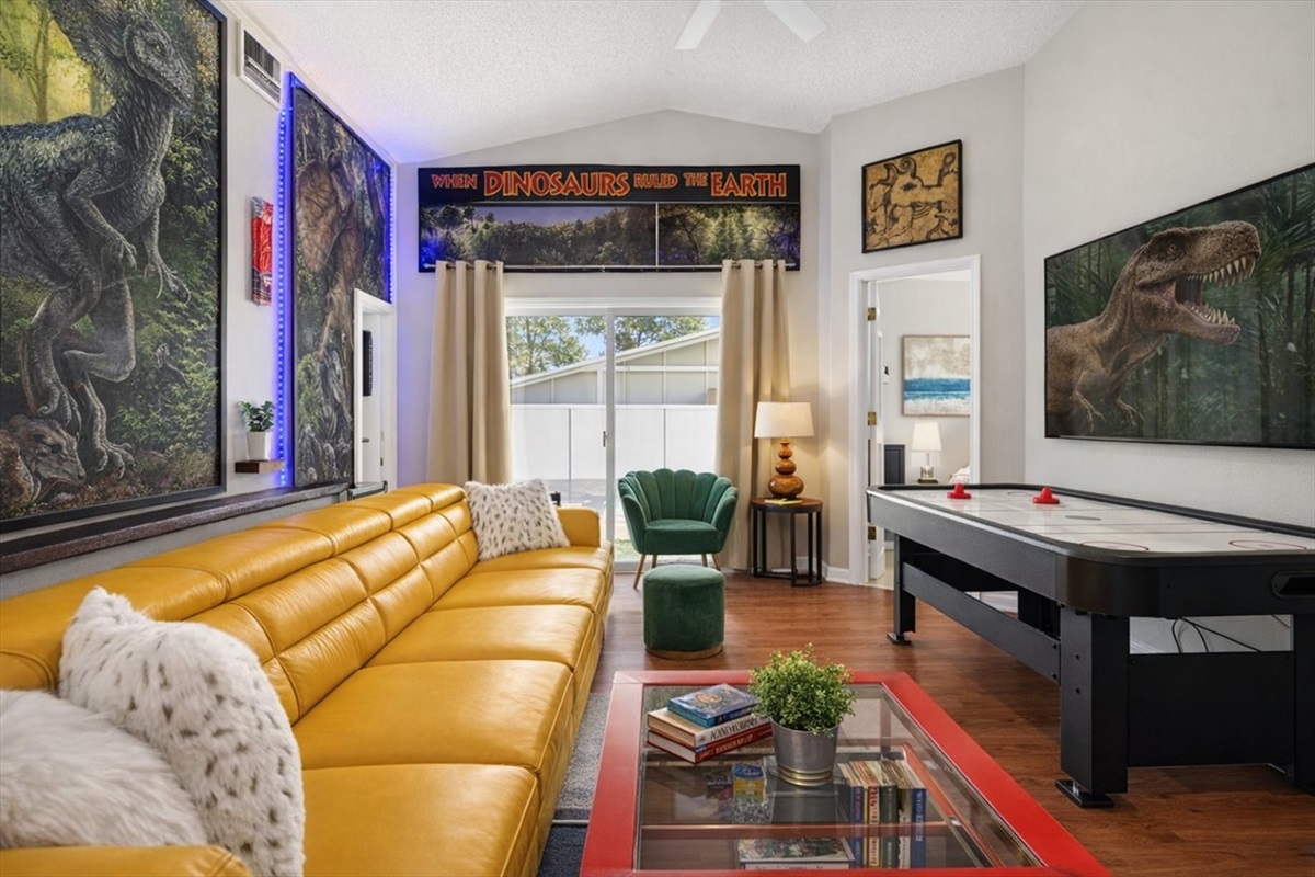 A modern living room featuring a yellow leather sofa and an air hockey table with dinosaur-themed decor.