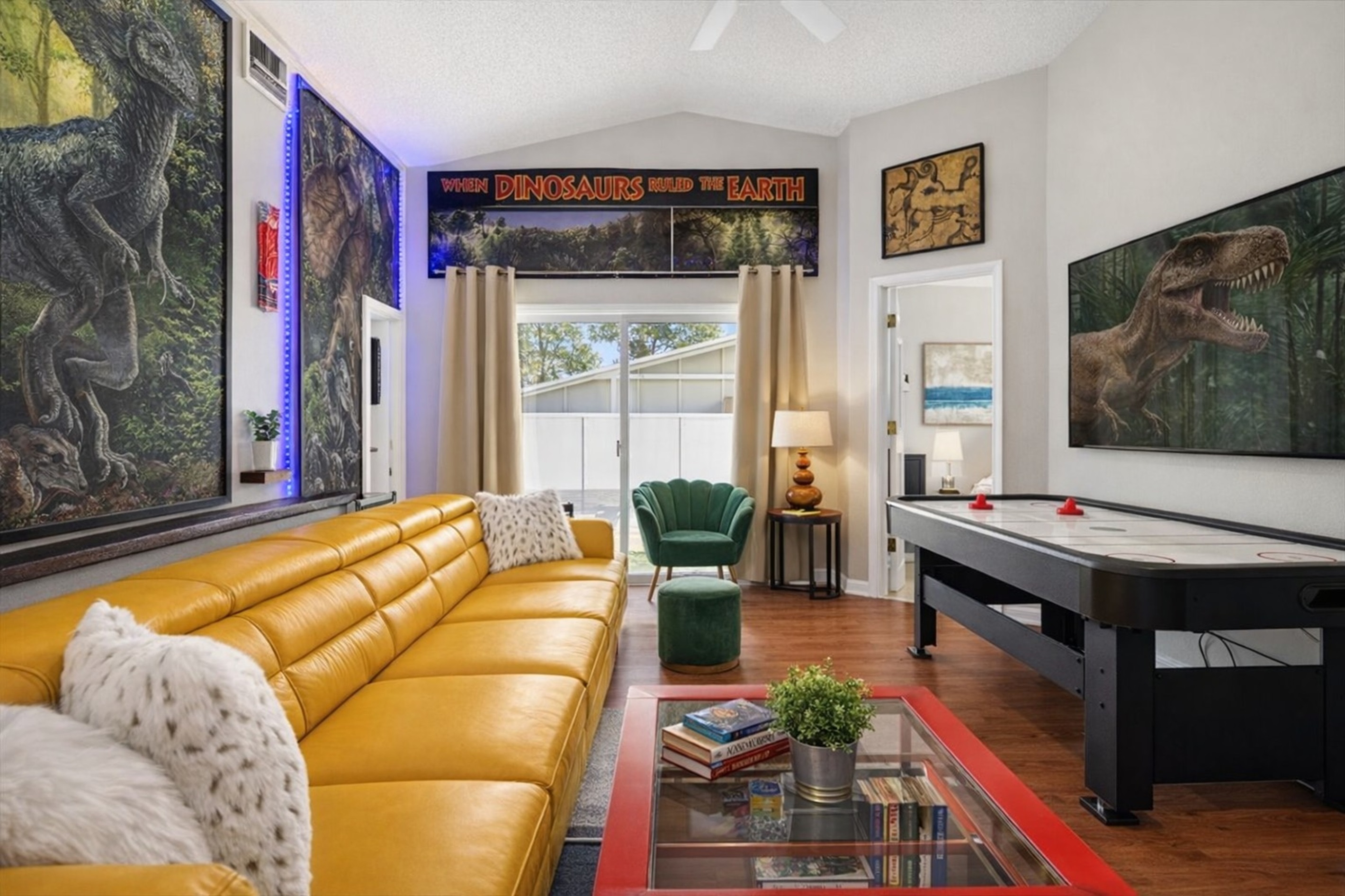 A modern living room featuring a yellow leather sofa and an air hockey table with dinosaur-themed decor.