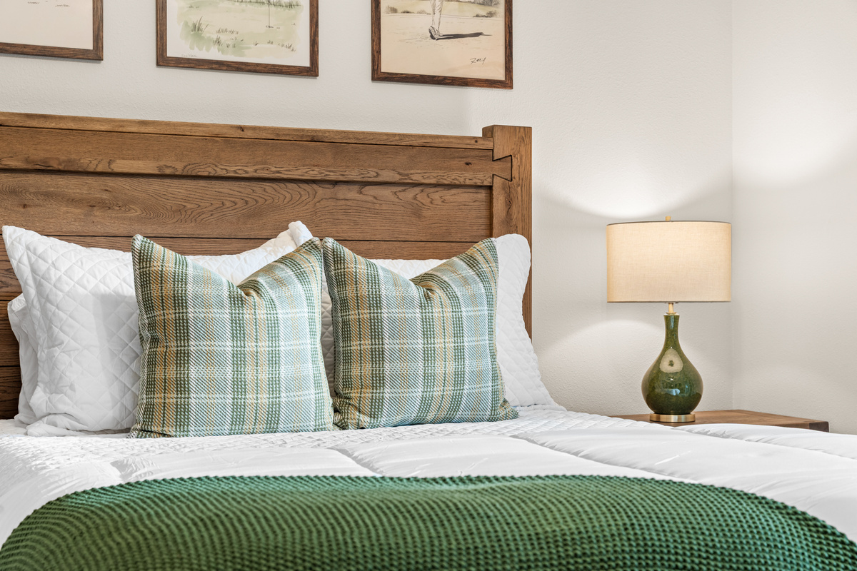 Sage plaid, a green knit throw, and a soft watercolor of the fairway above the bed.