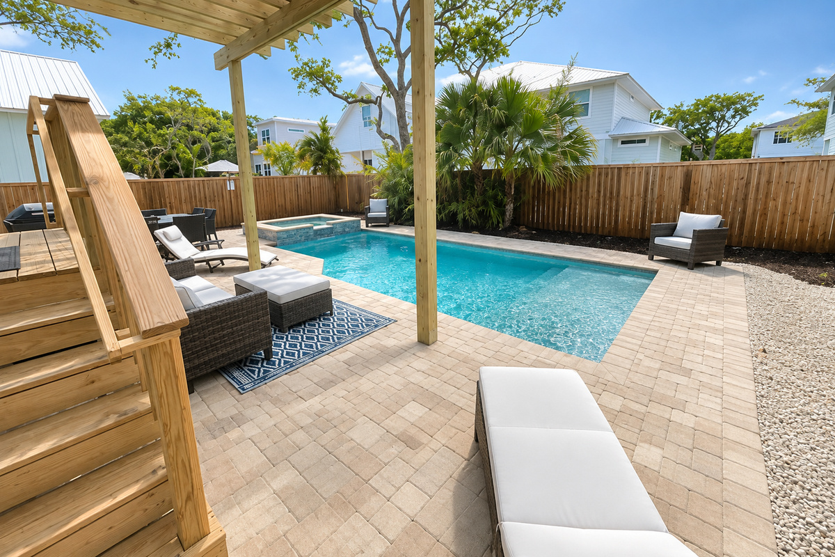 Every corner of the backyard earns its keep — pergola shade, poolside seating, a spillover spa in the corner, and wooden stairs connecting the porch to the party, all wrapped inside a private privacy fence.