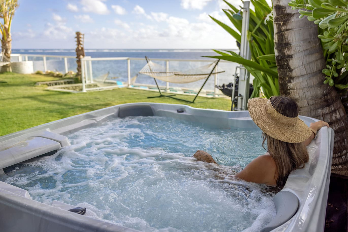 A state-of-the-art latest 7-person Jacuzzi-brand beachfront jacuzzi with full-body length lounger seats, cupholders and cushioned captain's headrests overlooking a crystal clear turquoise blue ocean.