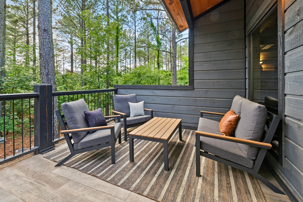 A balcony seating area with two cushioned armchairs and a central table, all set upon a striped outdoor rug