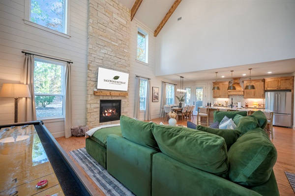 Bright, open-concept living room with vaulted ceilings, stone fireplace, and a large sectional—perfect for relaxing with family during your Broken Bow getaway. 🌲🔥