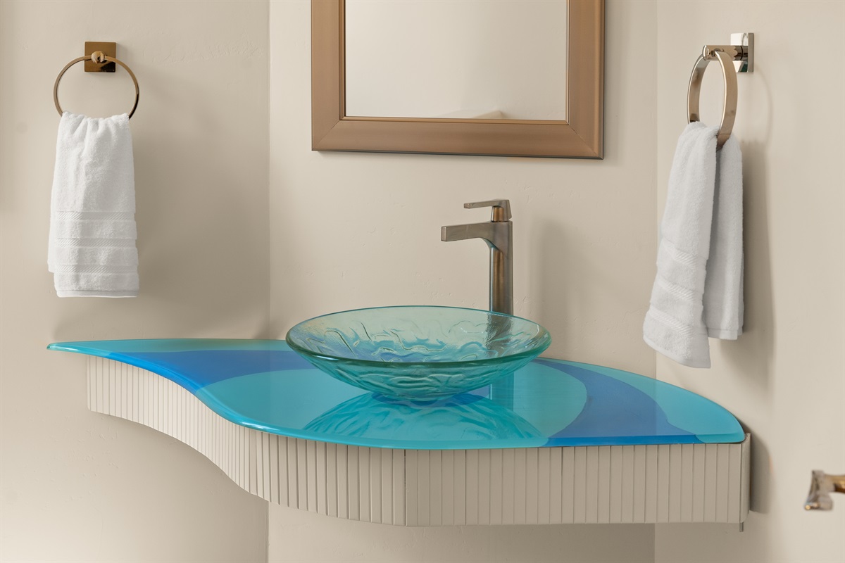 Unique, artistic design elements run throughout the home. This beautiful powder room features a custom sculpted glass vanity for an elevated touch.