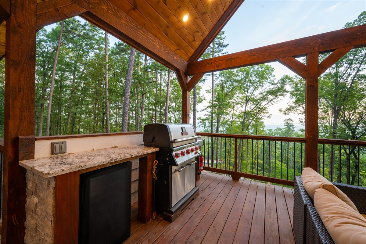 Outdoor grilling station with covered deck seating and forest surroundings