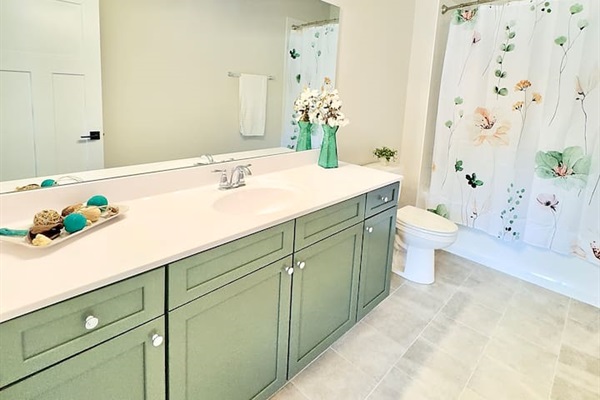 A spacious en-suite master bathroom, mirrors the serene color palette of greens and neutrals of the bedroom to offer a spa like retreat.