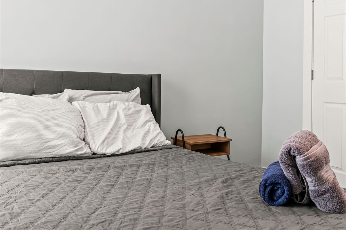 Clean and inviting sleeping area with full-size bed, folded towels, and convenient bedside storage.