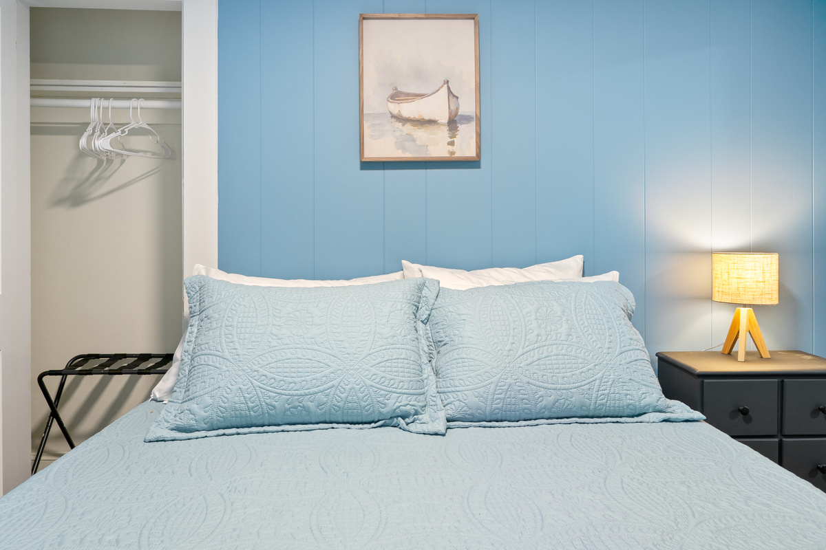 This head-on view of the queen bed showcases the functional layout of our second-floor sleeping space. Merging traditional Maine cottage charm with helpful guest utilities like a bedside closet and luggage rack, it delivers a deeply practical stay.