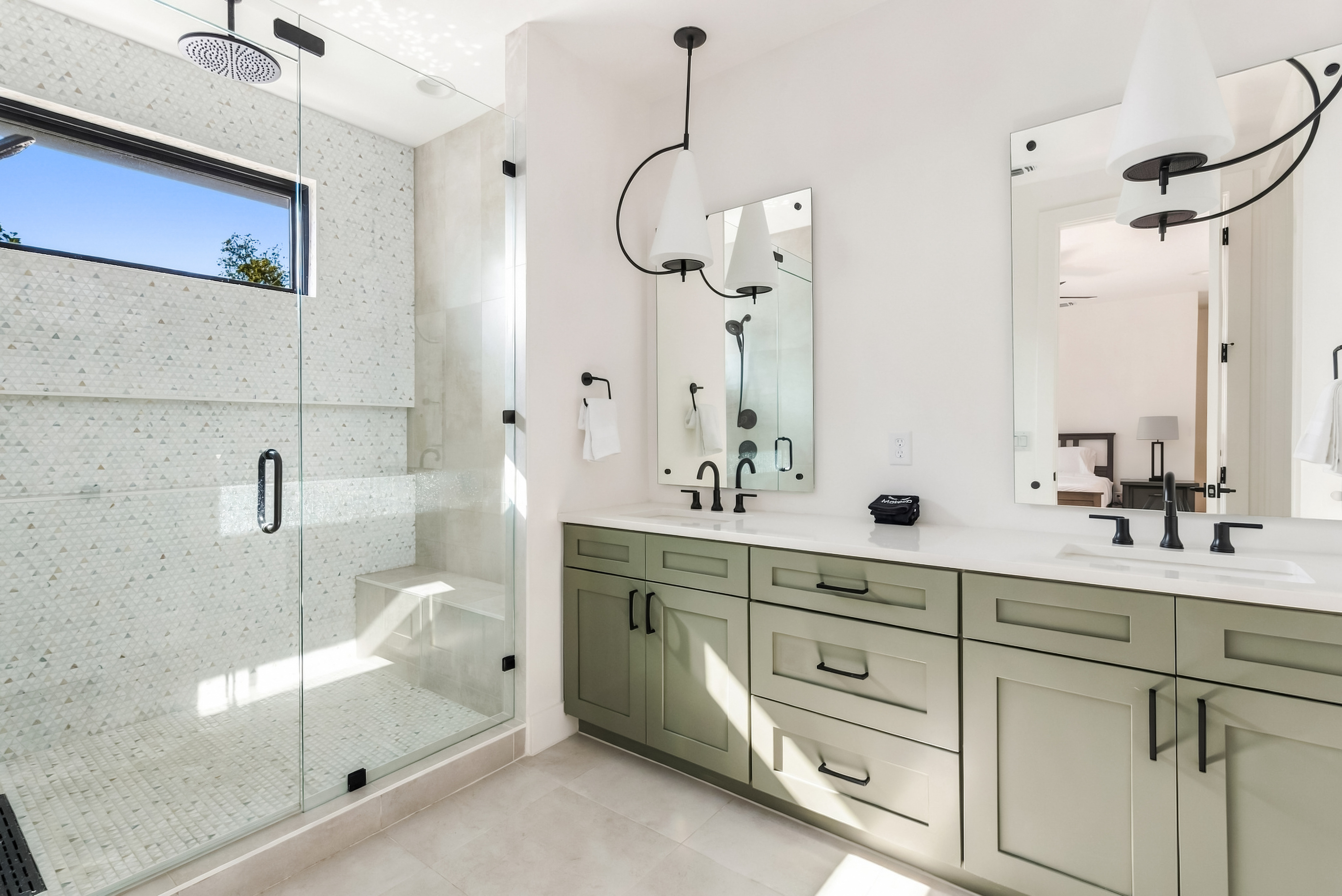 Glass walk-in shower and dual vanity, framed by soft green cabinetry.