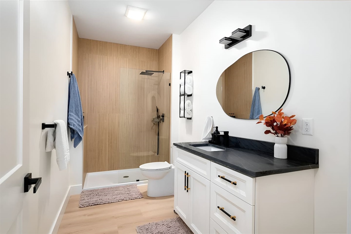Relax in this modern spa bathroom featuring a sleek black quartz vanity, a glass walk-in shower, and high-end matte black fixtures. This bright, luxury rental space includes an organic-shaped mirror and designer accents for a true boutique stay.