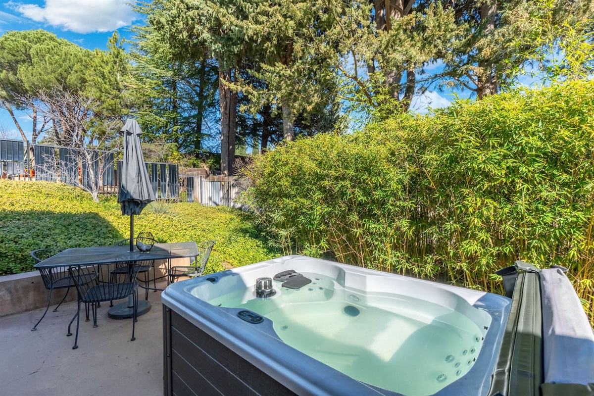 Secluded spa patio surrounded by lush greenery, featuring a hot tub and shaded dining area.