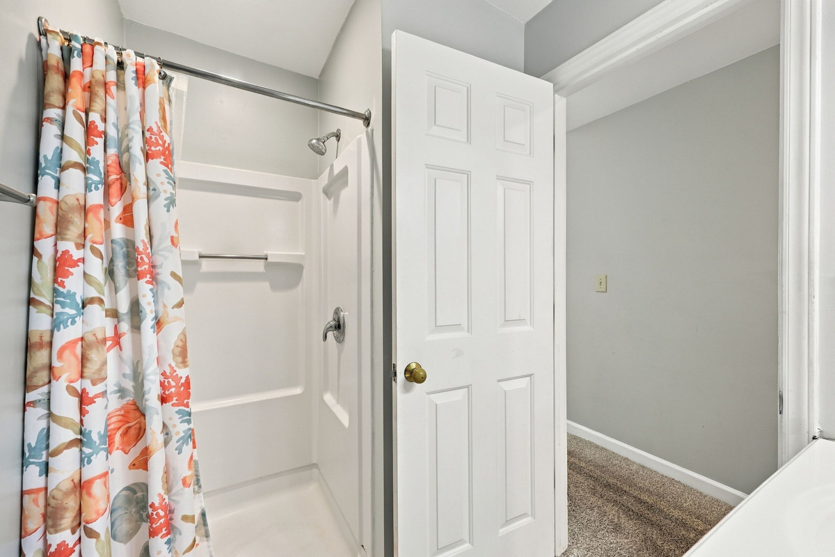 Coastal-chic guest bathroom shower area featuring a full step-in insert, brushed nickel hardware, soft neutral walls, and a vibrant ocean-coral motif shower curtain framing the doorway.   