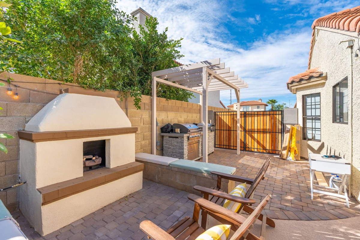 Multi-zone backyard with fireplace, pergola kitchen, loungers, and valley views—complete outdoor living and entertaining space.