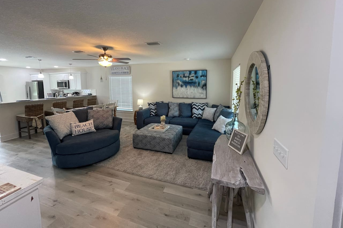 Ruby's Beach Paradise greets you the moment you walk in — a deep sectional built for pile-ons, a swivel chair for the storyteller, and an open floor plan that keeps the cooks, readers, and nappers happily connected.