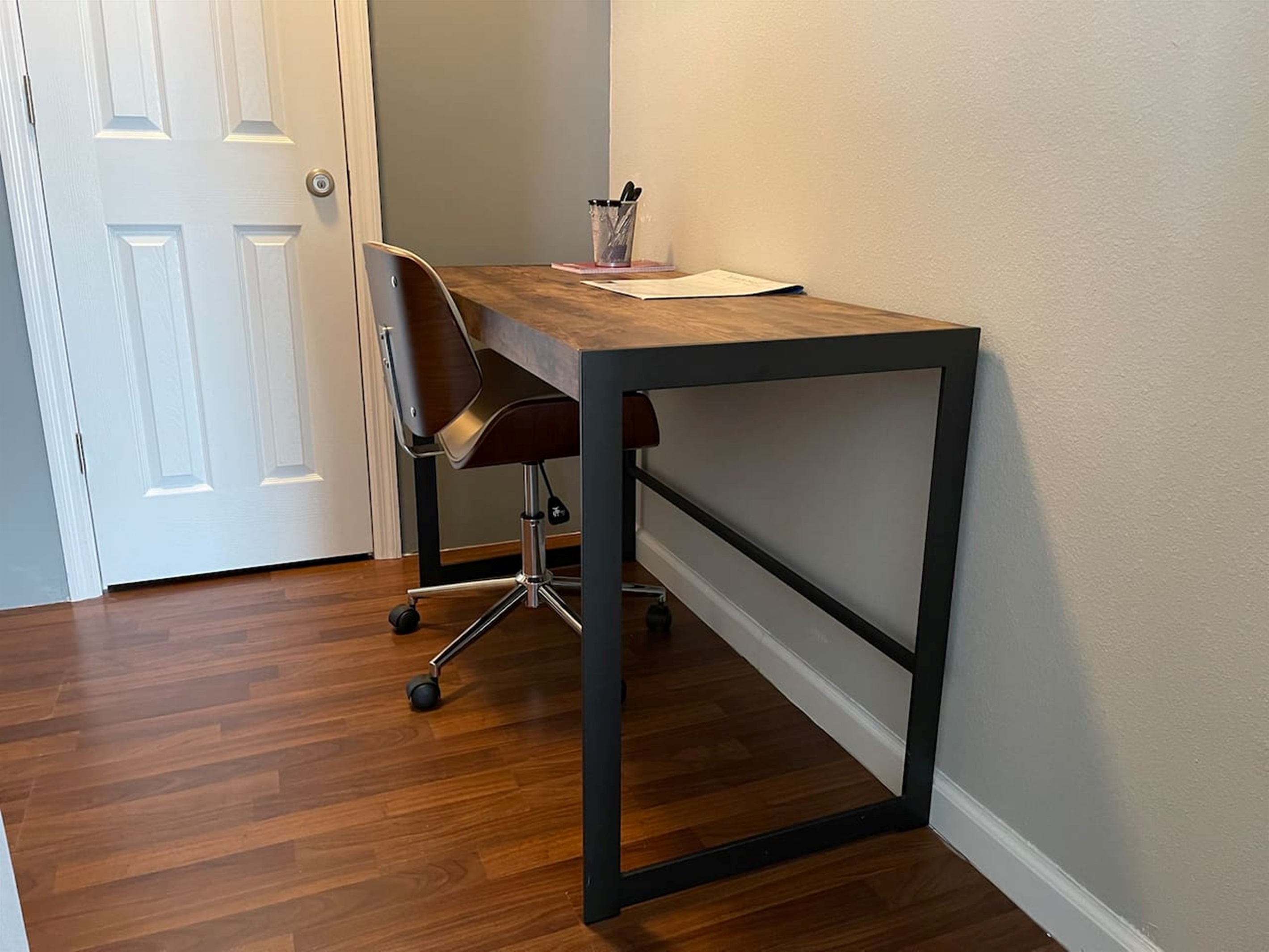 Functional workspace with a wooden desk and and office chair on hardwood floors.