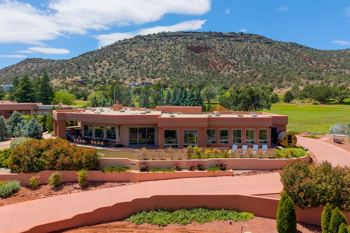 A spectacular aerial front view of Elara Retreats, perfectly framed by the iconic red rock formations and lush golf course greens of Sedona.
