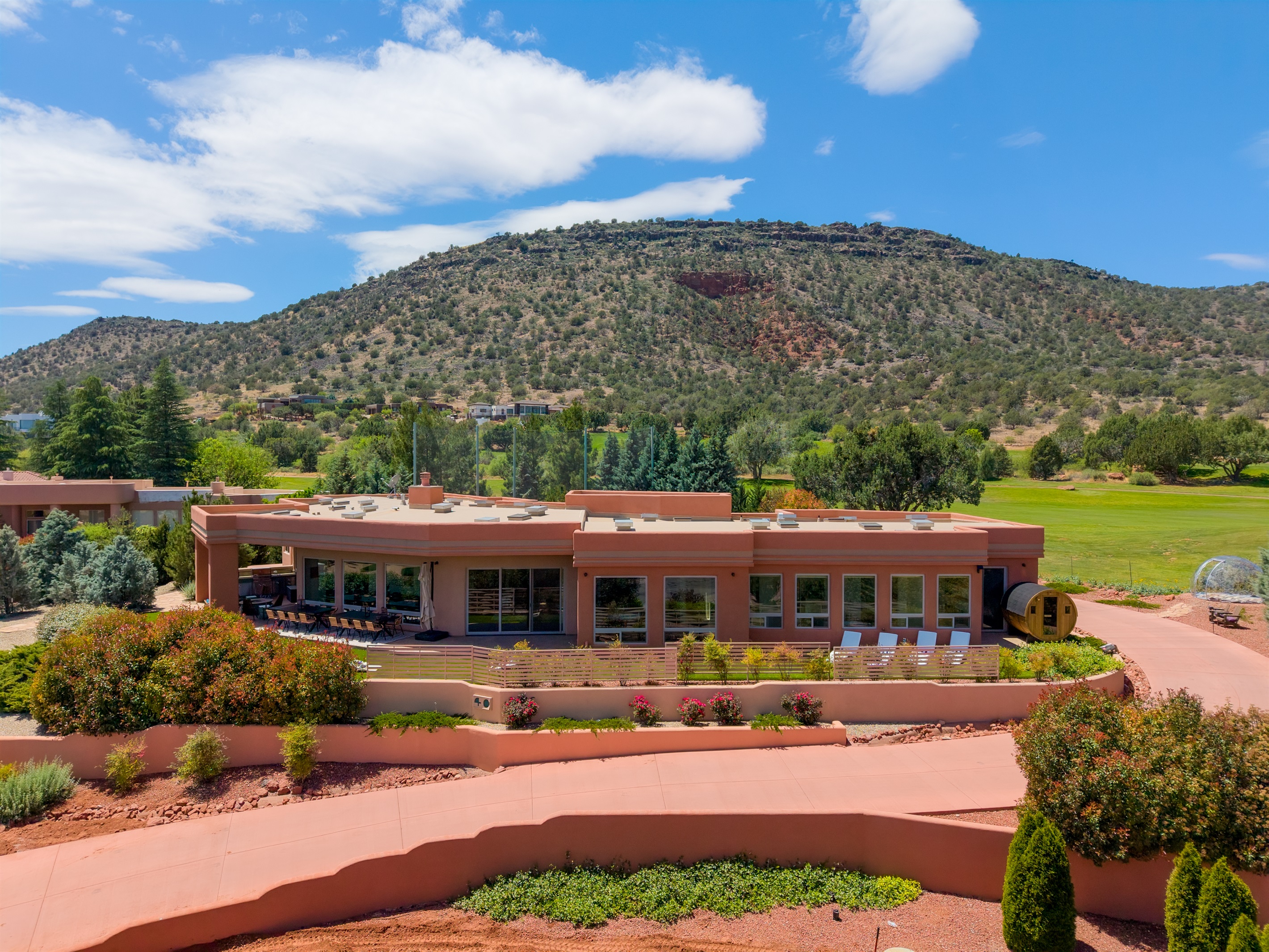 A spectacular aerial front view of Elara Retreats, perfectly framed by the iconic red rock formations and lush golf course greens of Sedona.