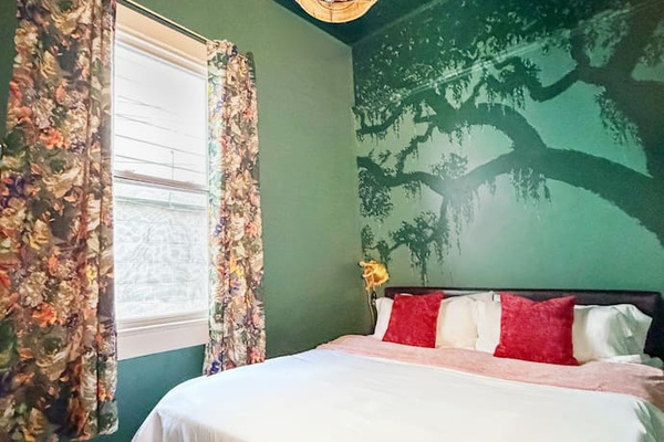 Moody green bedroom featuring a hand-painted Louisiana oak mural and starry night ceiling. A cozy, atmospheric space inspired by the magic of New Orleans. Features a king bed, plush linens, full-size mirror, a live oak mural, a secret speakeasy.