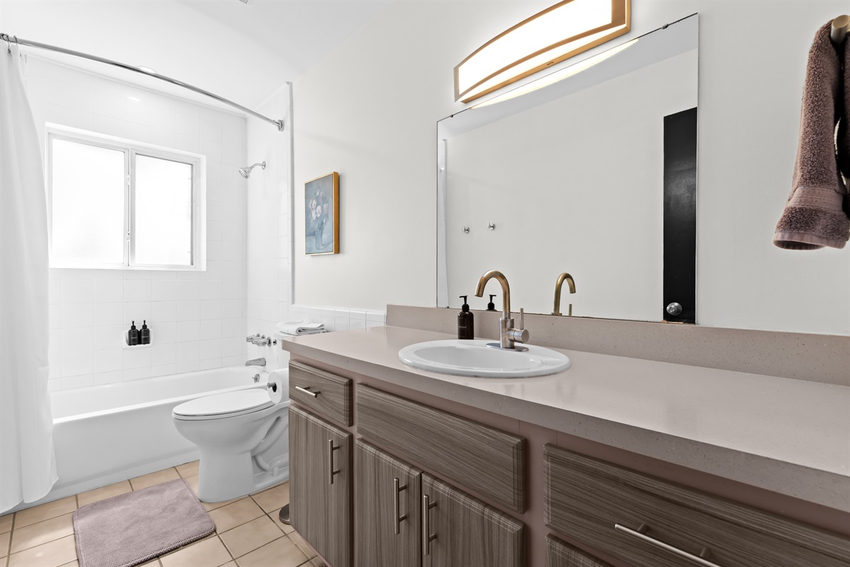 Clean and modern bathroom with vanity, large mirror, and full-size tub/shower.