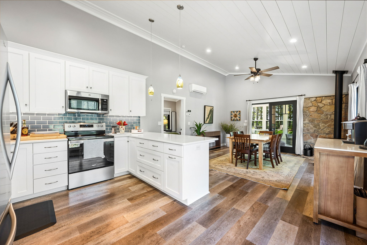 Cook and connect in the bright, fully-equipped kitchen featuring crisp white cabinetry, blue subway tile, stainless appliances, and an open flow to the dining area.