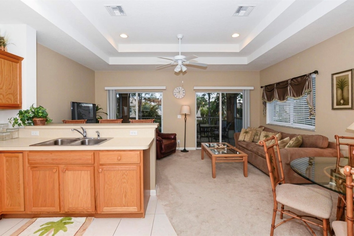 Spacious kitchen and living area with tray ceilings, breakfast bar seating, and sliding glass doors leading to the screened balcony.