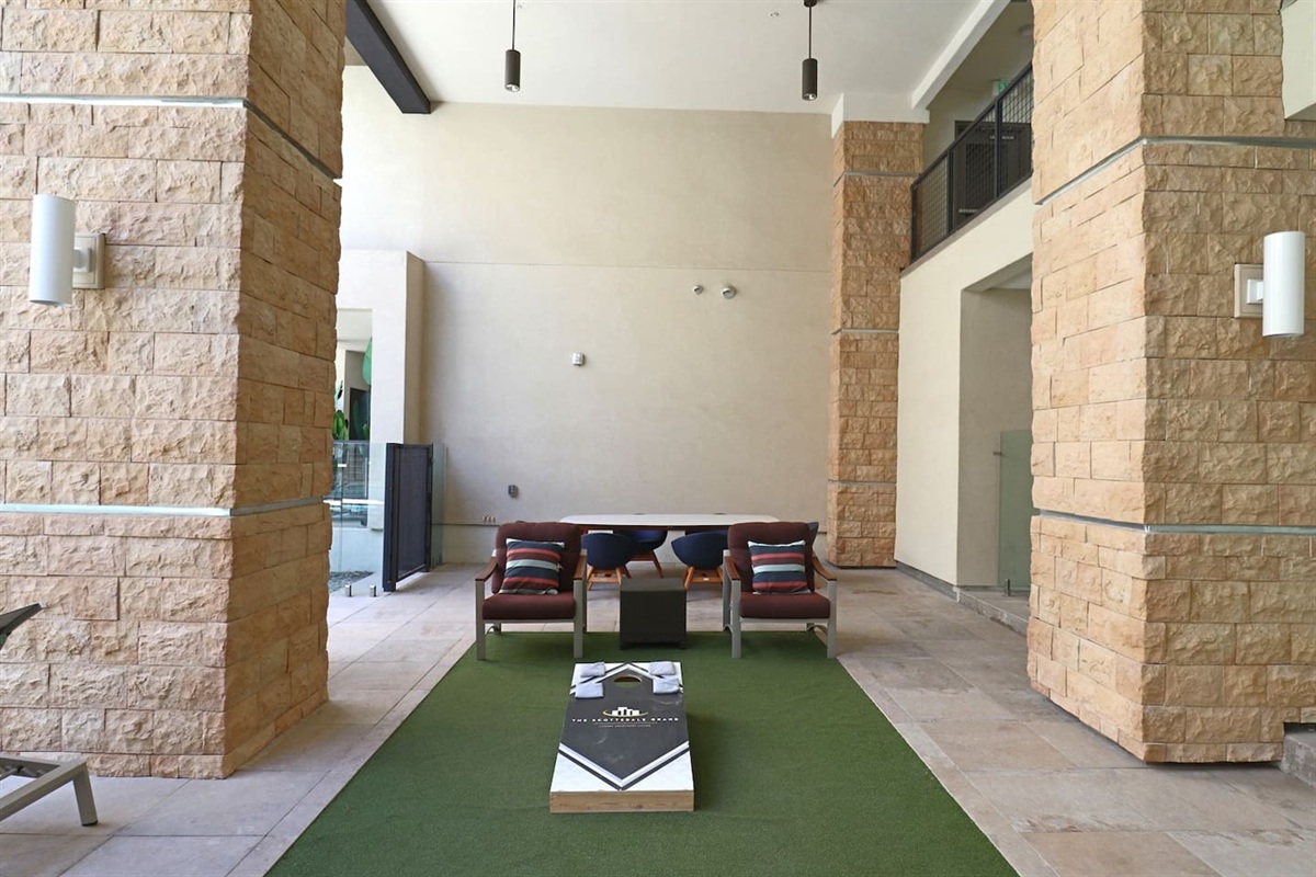 - Play and unwind in a shaded outdoor lounge with fun cornhole and seating   - Relax on comfortable chairs beneath tall stone columns and open-air design   - Perfect spot for casual games, friendly chats, or quiet afternoon relaxation