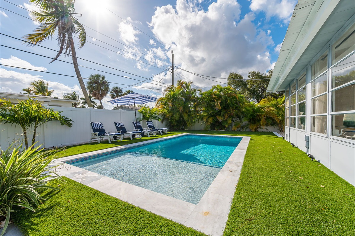 Dive into luxury with a sparkling heated saltwater pool, surrounded by lush palms, chic loungers, and modern turf for the perfect resort-style backyard escape.