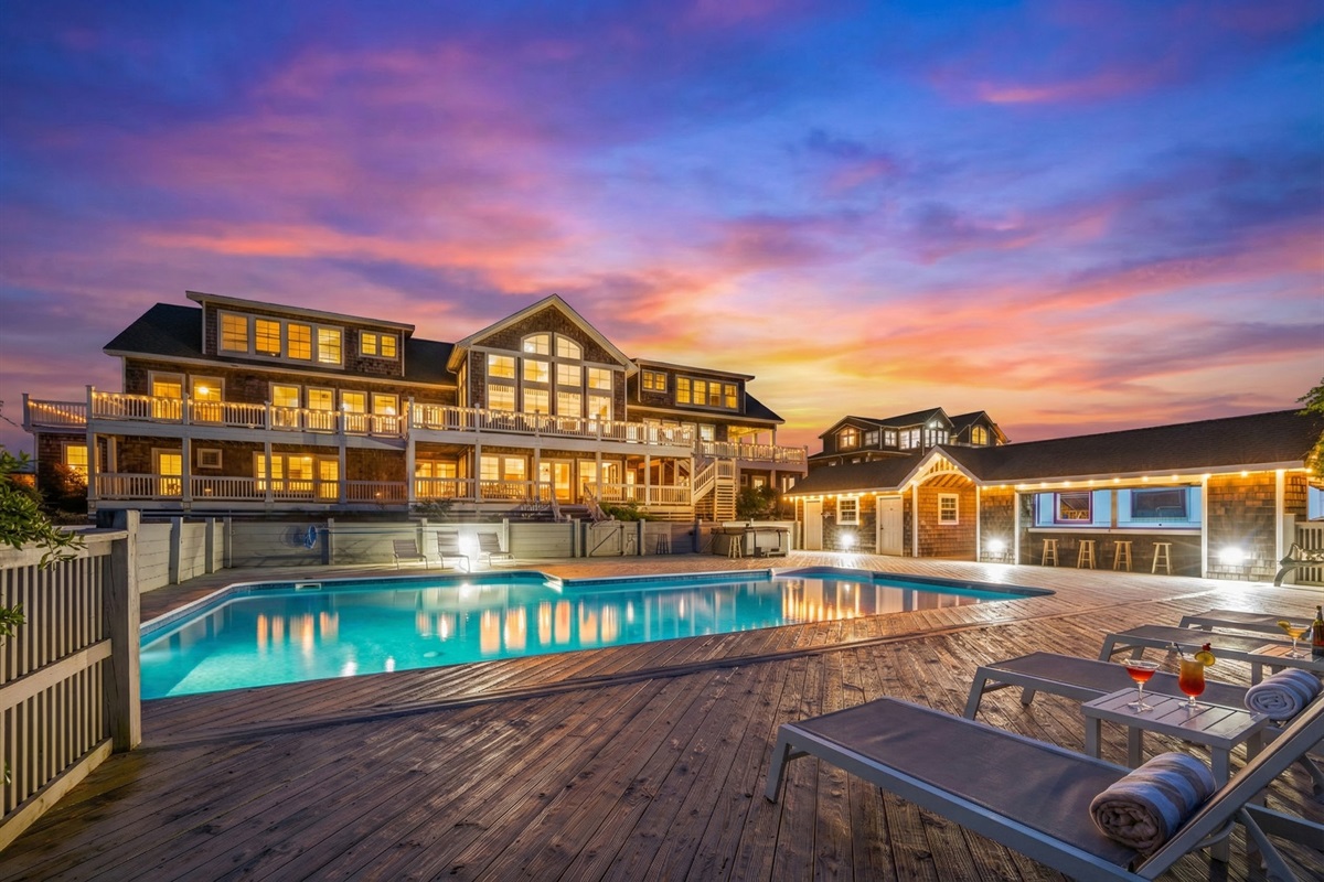 Spacious pool deck with lounge chairs and cocktails set against a colorful sunset.