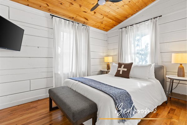 Guest bedroom offers a serene retreat with a queen-sized bed, crisp white linens, and a warm wood ceiling. Combining comfort and rustic charm.