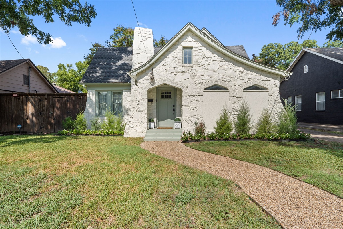 Historic 1929 stone cottage with curved driveway, mature trees, and manicured lawn. Northwest Dallas neighborhood minutes from Love Field Airport, the Design District, Uptown, and the Medical District. Free driveway and street parking on-site.