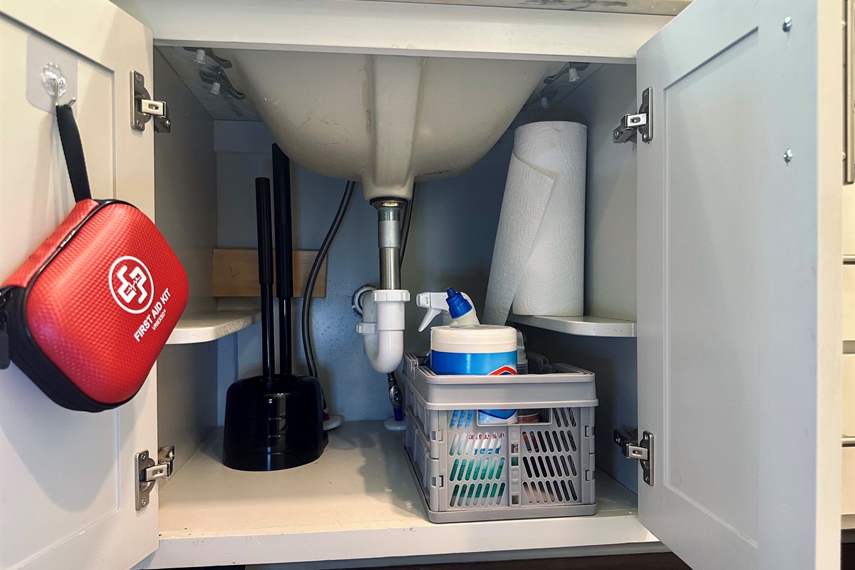 Left-side ensuite cabinet stocked with essential cleaning supplies, paper towels, and a conveniently placed first aid kit for added peace of mind.