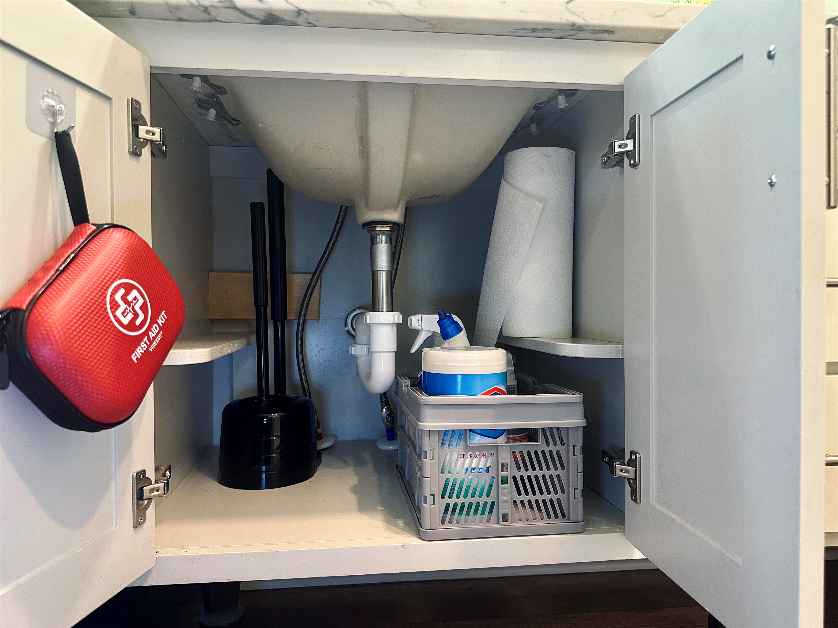 Left-side ensuite cabinet stocked with essential cleaning supplies, paper towels, and a conveniently placed first aid kit for added peace of mind.