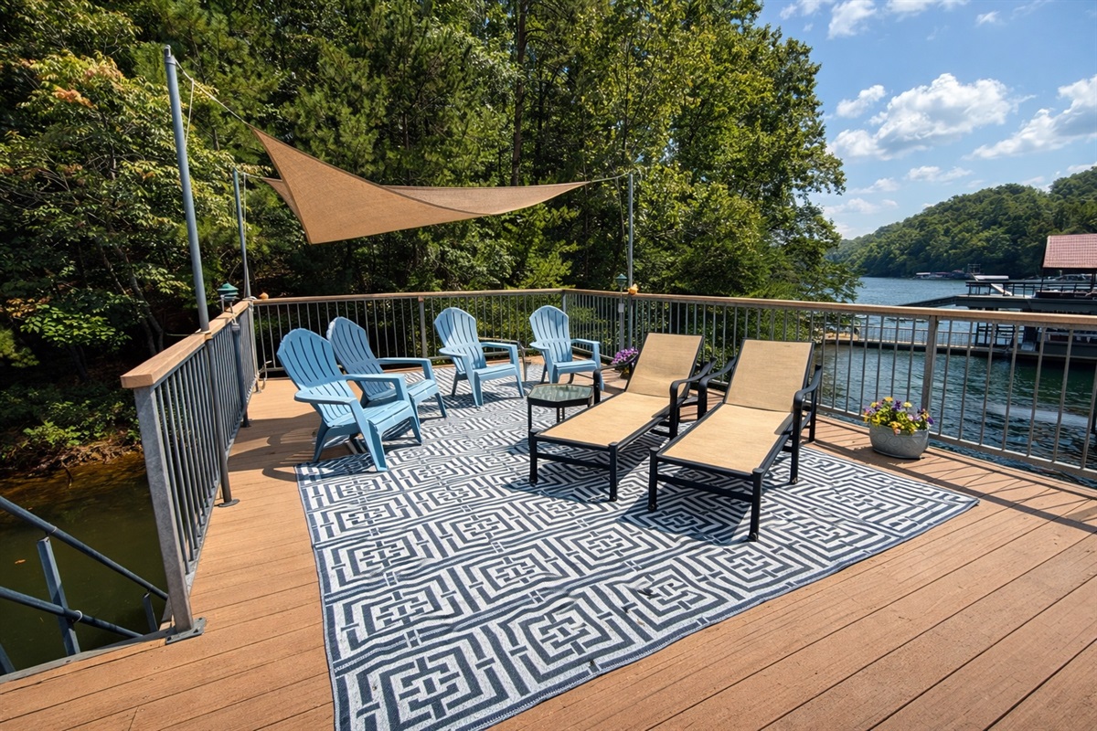 Spacious dock-top deck with shade sail, lounge chairs, and Adirondack seating overlooking the lake.