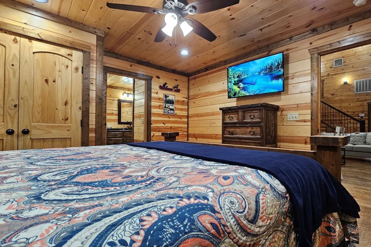 Bedroom 1: Relax in rustic charm with a plush bed and nature views through sunny windows!