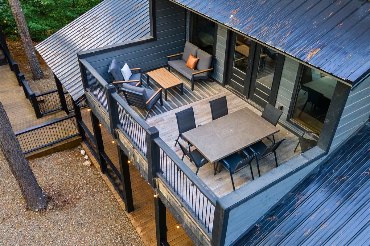 a modern cabin with spacious deck and dining area surrounded by trees.