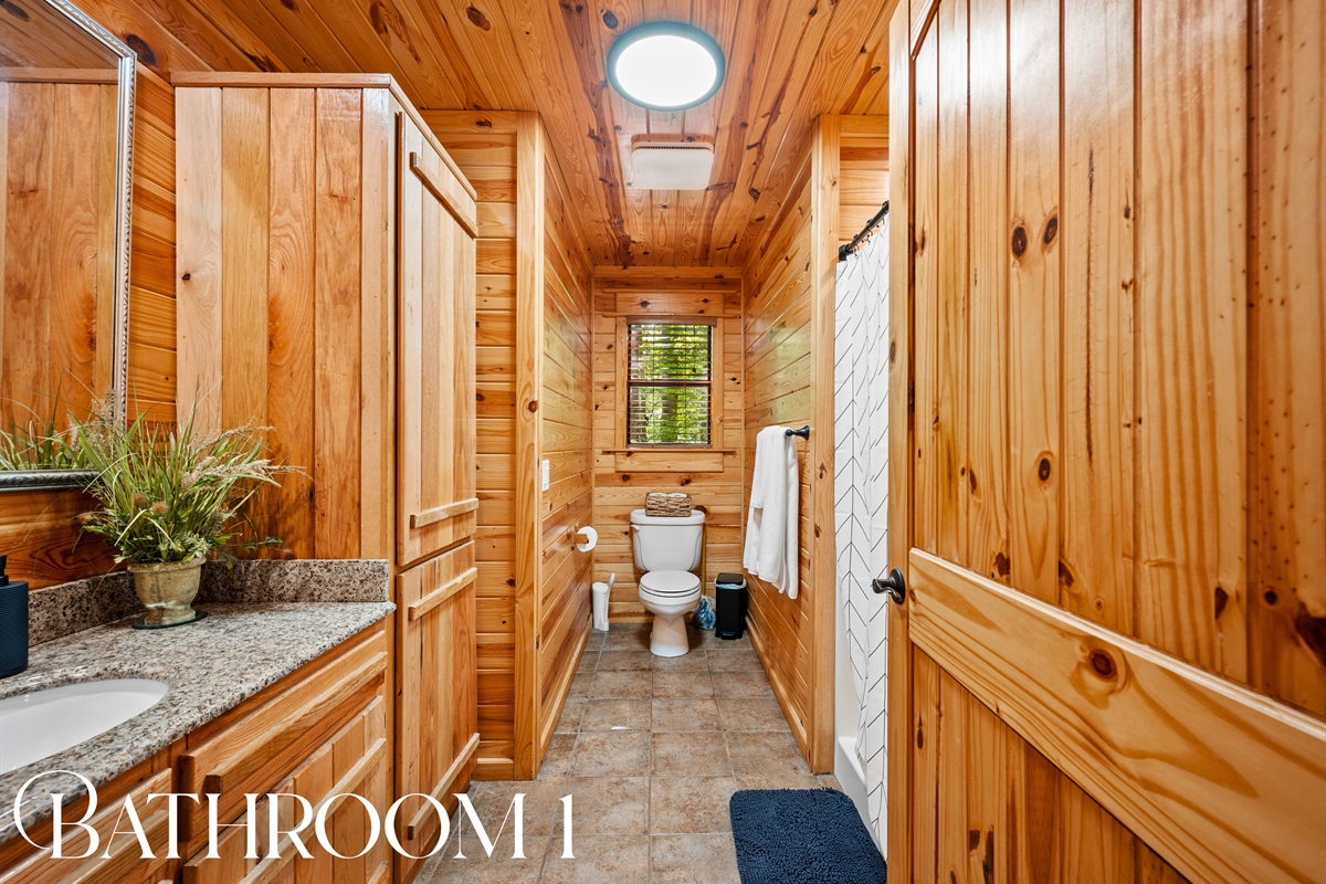 Bathroom 1 with extended granite vanity, natural wood finishes, and spacious layout for guests or shared use.