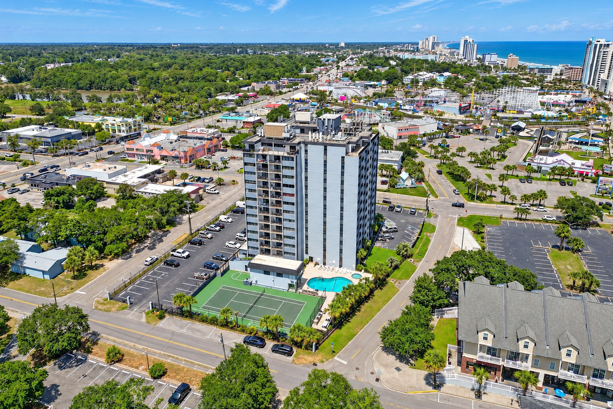 Aerial view of Holiday Towers with shared pool, hot tub, sports court, parking, and Myrtle Beach attractions nearby.
