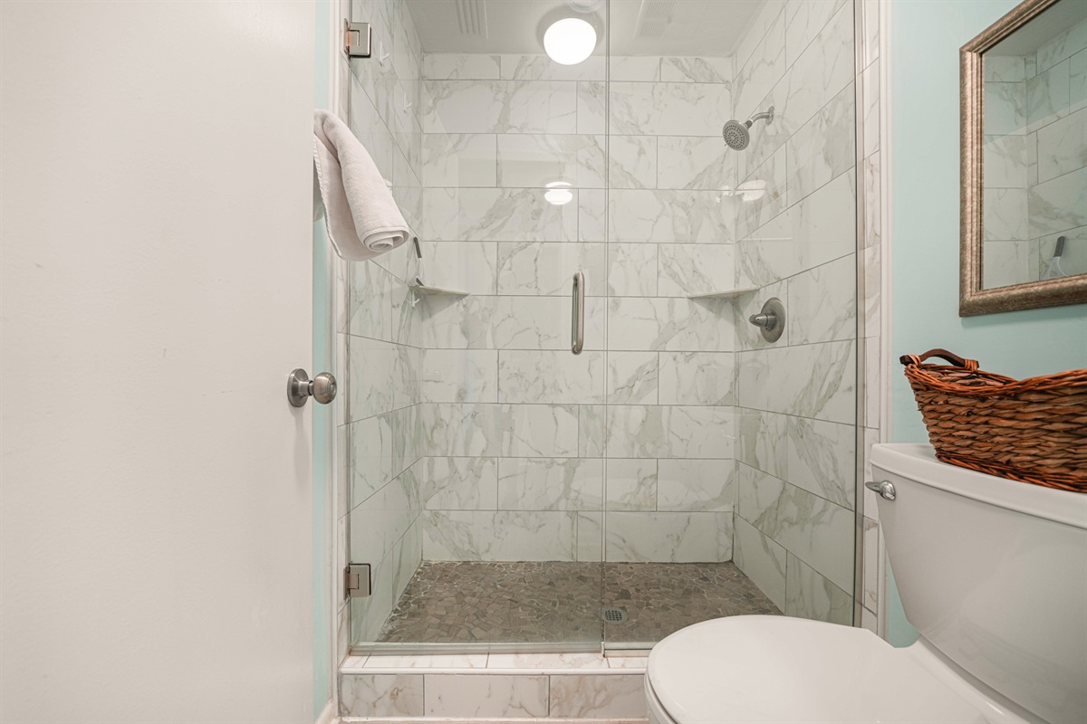 Spa-worthy shower in the master bath. Marble tile walls, pebble stone floor, and a frameless glass enclosure — a cut above most rentals.