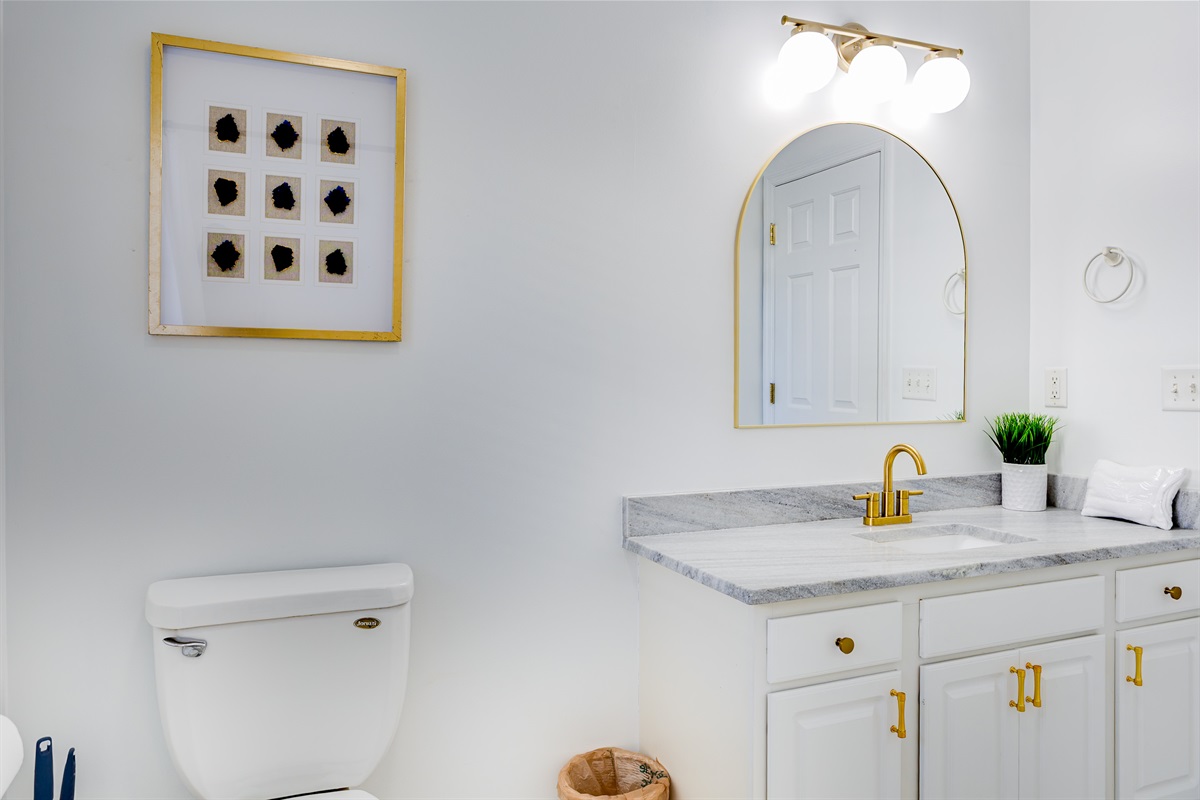 Bright and elegant master bath with a marble vanity, brushed gold fixtures, arched mirror, and ample counter space