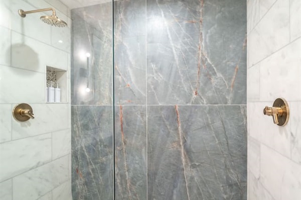 Luxury ensuite bathroom with brass fixtures, and a large spa-style walk-in shower with glass enclosure and floor-to-ceiling stone tile. Plus, heated marble floors! 