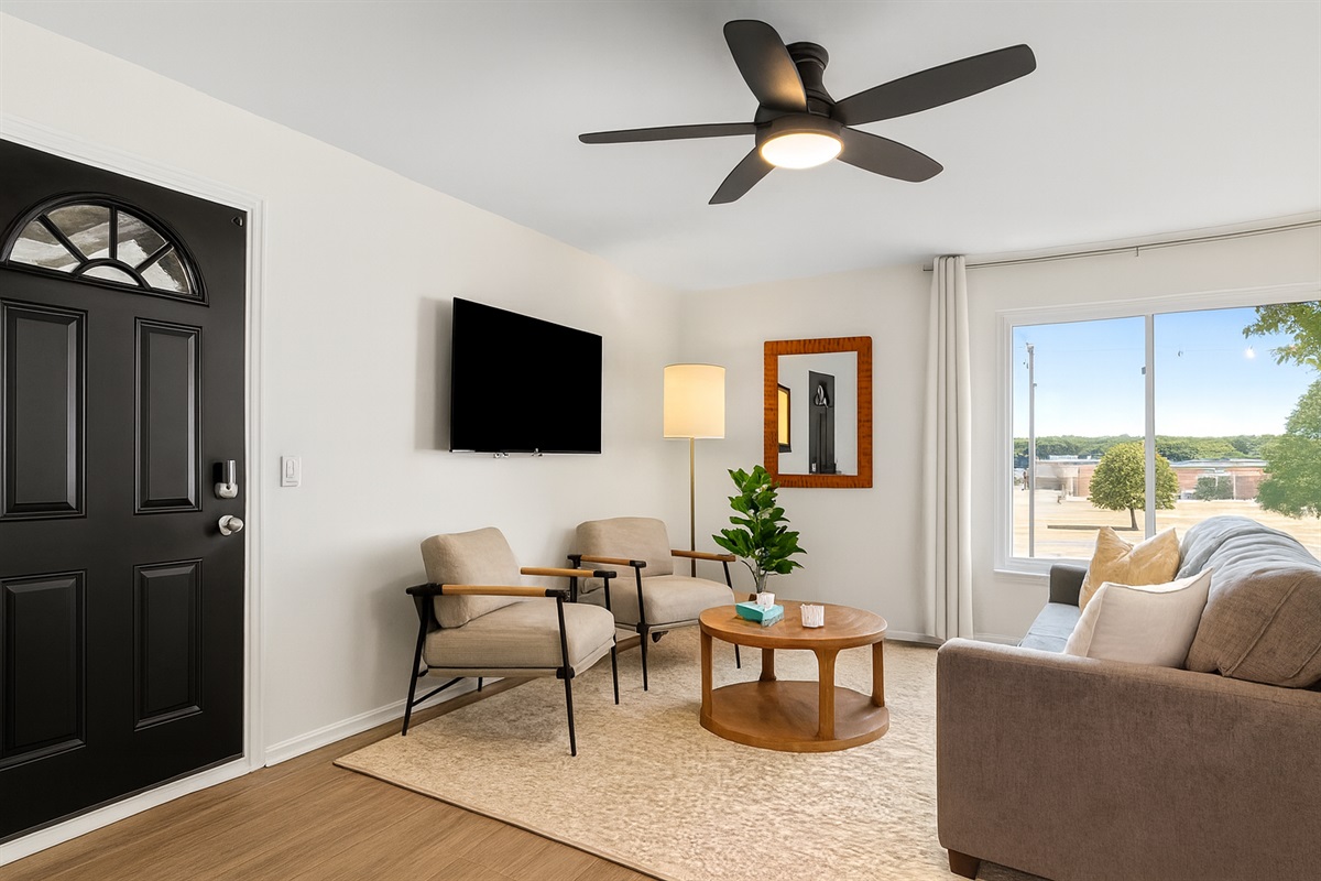 Relax in this sunlit living room, complete with a comfy sofa, leafy views, and a large Smart TV.