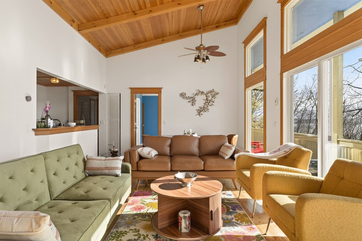 Sun-filled living room with soaring ceilings, warm wood accents, and floor-to-ceiling windows overlooking Canandaigua Lake—enjoy cozy seating, natural light, and seamless access to the balcony for relaxing mornings or peaceful evenings