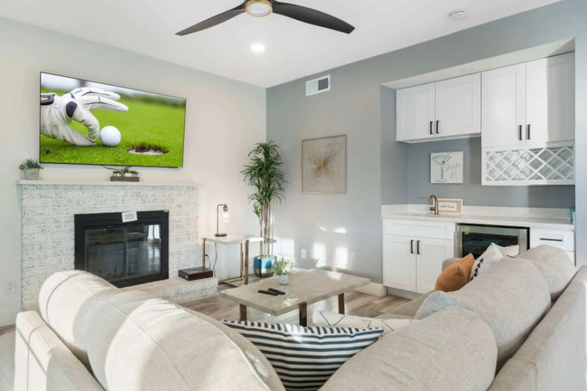 Light-filled living room with fireplace, bar, smart TV, and dual seating areas.