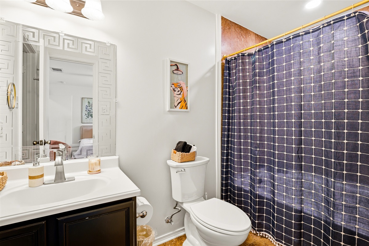 Full bathroom with tiled shower and tub combo, gold curtain rod, decorative framed mirror, and dark wood vanity. Stocked with Ginger Lily Farms shampoo, body wash, conditioner, and fresh towels.