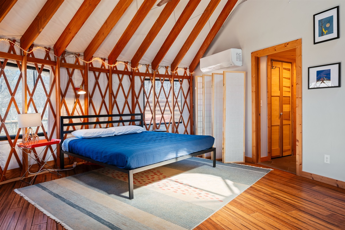 Main Floor King Bed Caption:
Open-concept main floor king sleeping area located beside the bathroom, featuring a privacy divider for added separation while maintaining the cozy charm of the yurt.