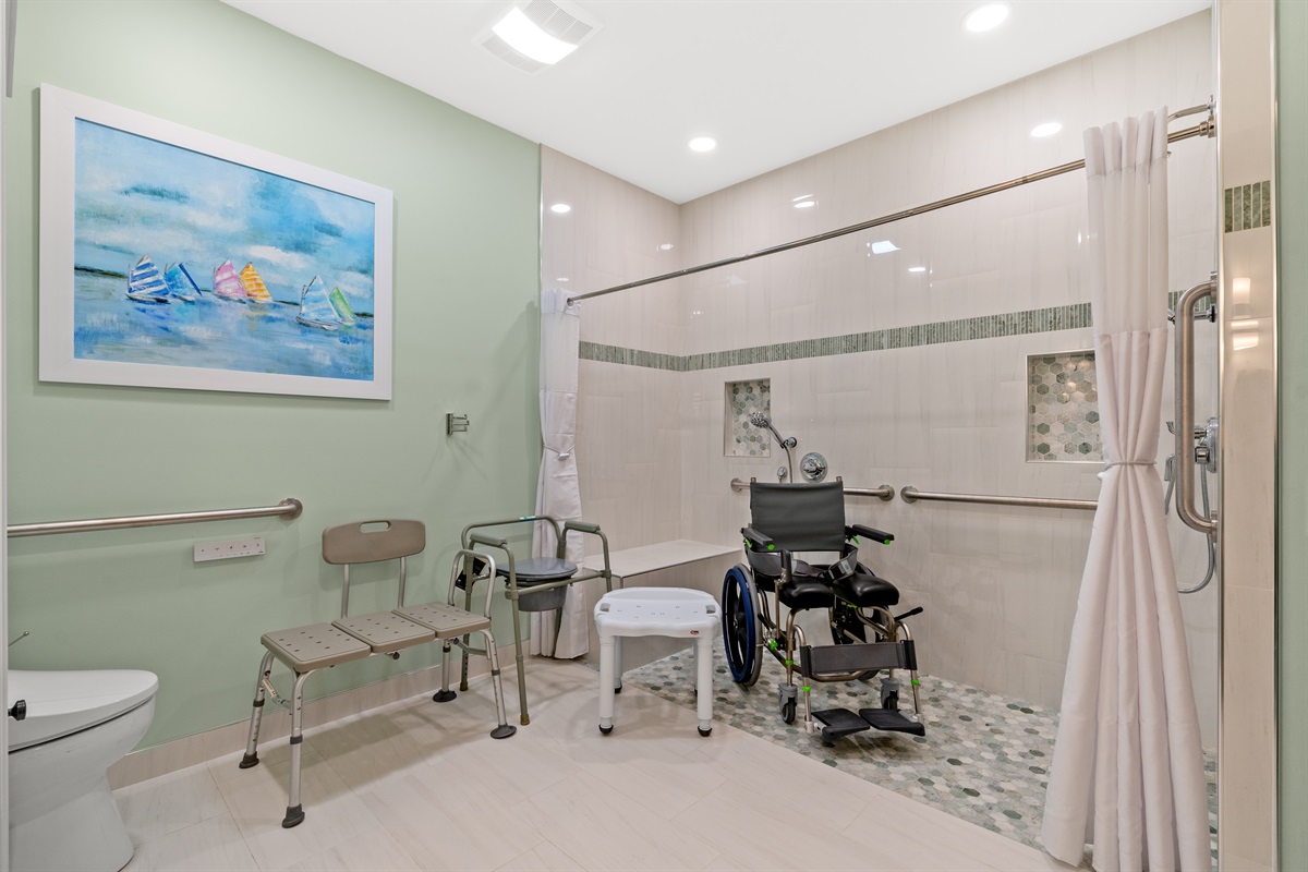 Barrier free roll-in shower with shower bench, shower chair, grab bars and hand held shower sprayers.