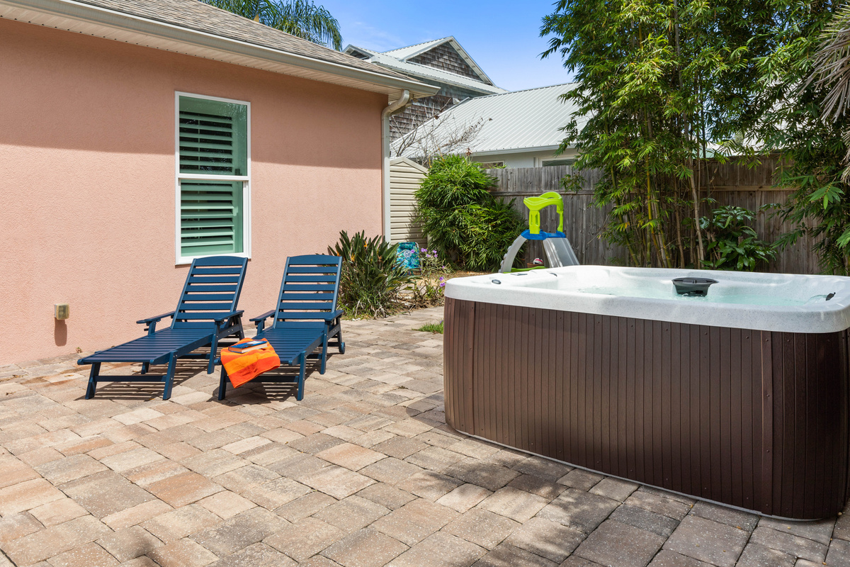 Hot tub beside two navy chaise loungers, with the toddler slide just behind it, so parents can soak and keep watch.
